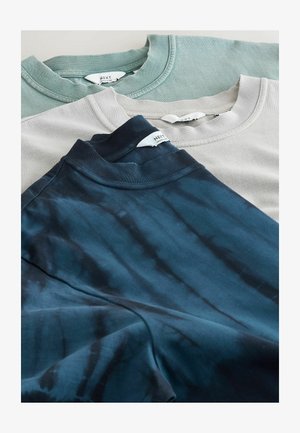 Drei übereinandergelegte T-Shirts: eines hellgrün, eines hellgrau und eines navy-blau mit Batikmuster, alle mit Rundhalsausschnitt und sichtbaren Markenetiketten am Kragen.