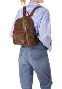 Sac à dos en cuir marron avec une forme arrondie, doté d'une poche zippée à l'avant, de deux bretelles et d'une surface texturée.