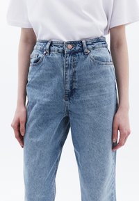 Valkoinen denim korkea vyötäröiset farkut rento malli, joissa on viisi taskua, kuparinväriset napit ja kevyttä kulutusta.