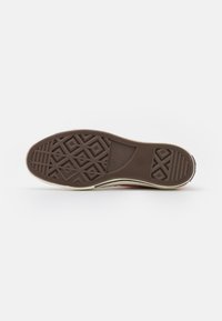 Solares de borracha castanha com um padrão de agarrar texturizado, com uma borda bege e detalhes brancos na entressola. Marca "Converse All Star" visível.