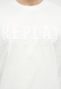 Λευκό μπλουζάκι με ανάγλυφα λευκά γράμματα "REPLAY" και μικρότερο ανάγλυφο κείμενο "EIGHTYONE" στο στήθος.