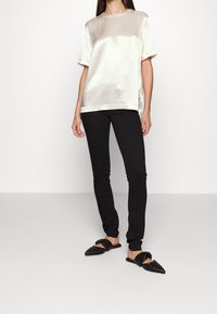 Top corto in raso crema con maniche a sbuffo, caratterizzato da un collo rotondo e fessure laterali, abbinato a jeans skinny neri e mule nere con punta.