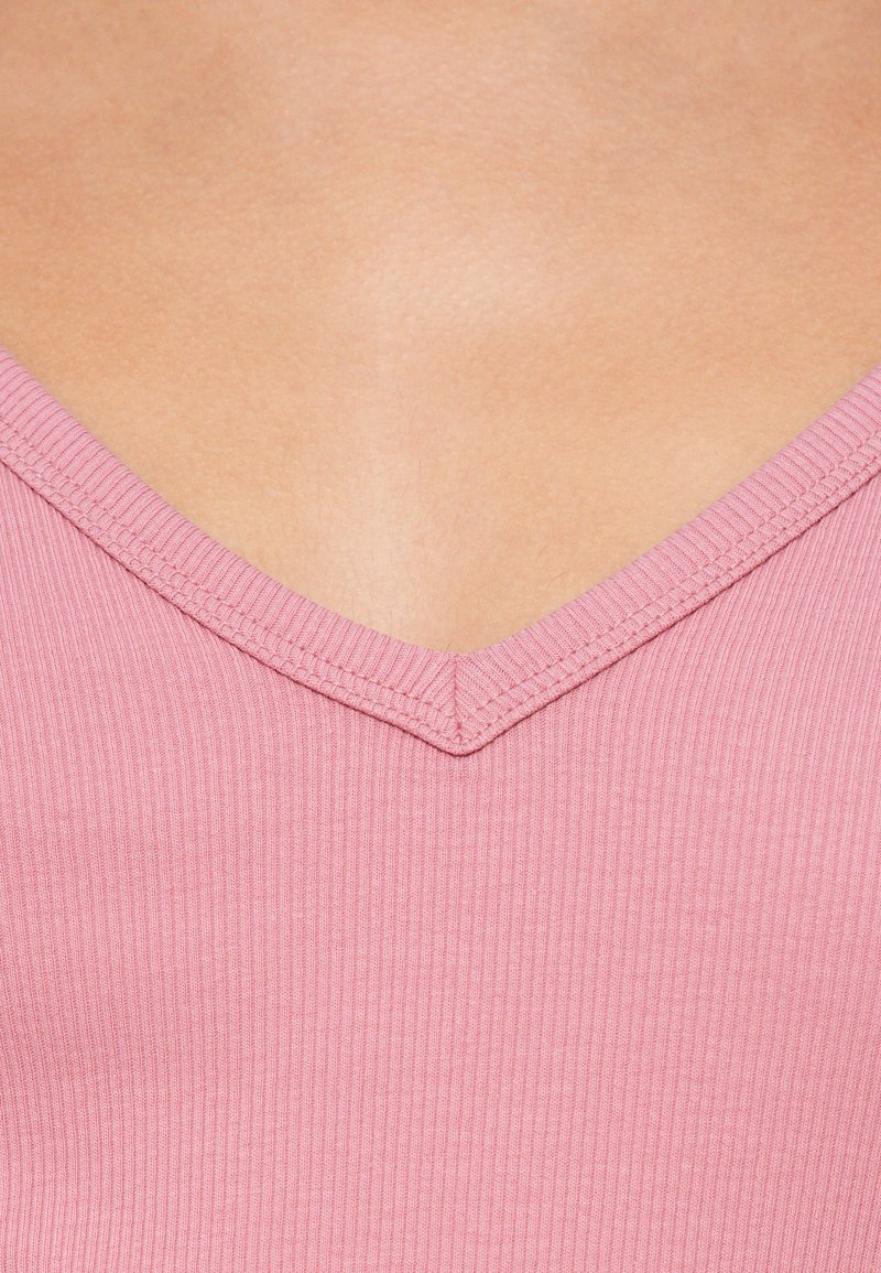 Rosa geripptes V-Ausschnitt-Oberteil mit strukturierter Oberfläche. Der Ausschnitt zeichnet sich durch eine klare, definierte Kante aus, die das minimalistische Design des Kleidungsstücks betont.