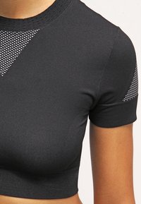Acercamiento de una persona que lleva una camiseta corta de manga corta negra con detalles de malla texturizada en el escote y las mangas.