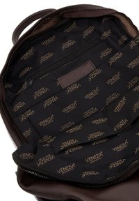 Intérieur d'un sac à dos en cuir marron avec une doublure en tissu noir présentant un logo doré "VENEZIA" répété et une poche zippée.