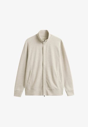 Lichtbeige jas met rits, hoge kraag, lange mouwen en twee zijzakken, weergegeven op een witte achtergrond.