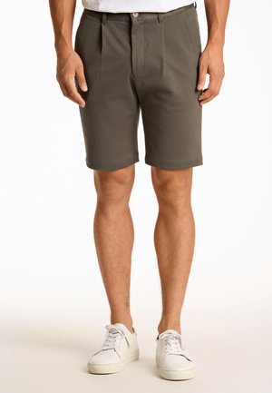 Donkergrijze shorts met een vlakke voorkant, geplooid ontwerp en opgerolde zomen, gecombineerd met witte sneakers, op een effen achtergrond.