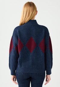 Maglione in maglia blu navy con motivi a rombi color granata, collo e polsini a coste. Tessuto strutturato e vestibilità rilassata, adatto per essere indossato a strati.