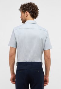 Camicia azzurro chiaro a maniche corte con pattern a quadri, colletto button-down e una texture liscia; abbinata a pantaloni navy scuri con tasche posteriori.