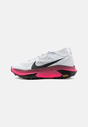 Chaussure de course Nike blanche avec un swoosh noir, semelle épaisse rose et noire, et étiquettes "zoomX" et "vibram" sur la semelle.