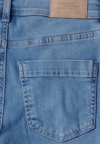 Jeans in denim azzurro chiaro con una sola tasca posteriore e dettagli cuciti. Presenta un'etichetta in pelle sulla cinturina con il nome del marchio impresso.