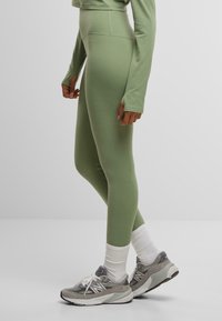 Green high-waisted leggings with a smooth texture and fitted design, paired with gray sneakers and white ankle socks.