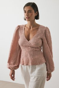 Blusa rosa ricamata con maniche lunghe e puffate e scollatura a V profonda; tessuto testurizzato con motivi floreali. Vita semplice e aderente.