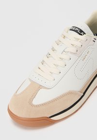 Sneakers bianchi in pelle con accenti in suede beige, punta rotonda, lacci piatti color crema e suola in gomma marrone. Presenta il logo del marchio sulla linguetta.