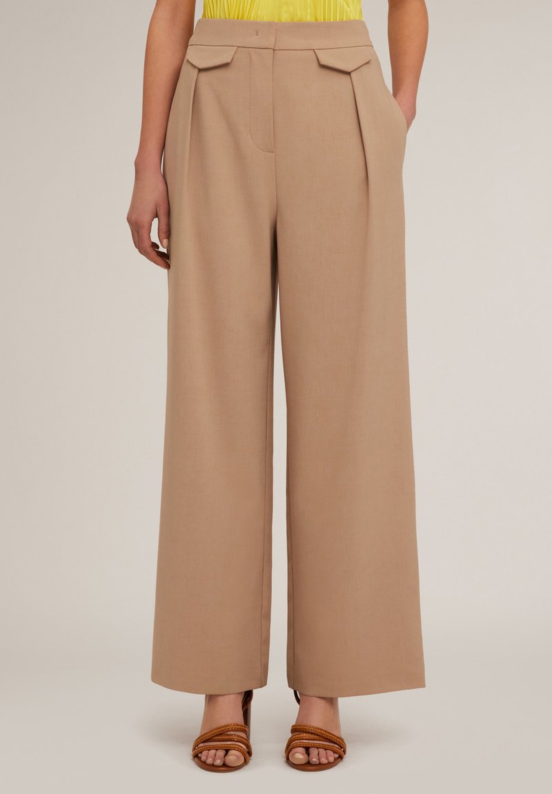 Beige wijde broek met voorplooien, zijzakken en een zachte textuur, gecombineerd met bruine sandalen met bandjes.