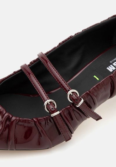 Burgundi színű, patent balerina cipő, gyűrt dizájnnal, két állítható pánttal ezüst csatokkal és texturált fekete belső résszel.