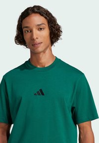 Zöld pamut póló, fekete hímzett logóval a mellrészen. Rövid ujjú és kerek nyakú. Sima textúra.