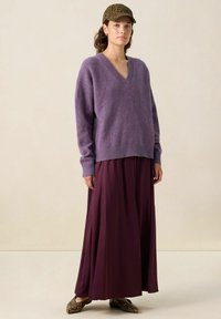 Pull violet en V avec une coupe décontractée et un ourlet côtelé, associé à une jupe maxi bordeaux fluide et des ballerines à imprimé serpent. Casquette marron à motifs léopard.