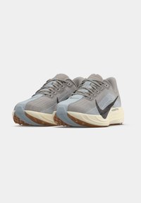 Par de zapatos deportivos para correr en tonos gris y azul claro con logo de swoosh negro, medias suelas blancas y suelas de goma marrón sobre fondo blanco.