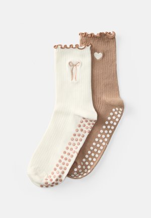 Zwei Paare gestrickte Socken: eines in Creme mit einem Schleifenmuster und rosa Punkten, das andere braun mit einem Herzmuster und weißen Punkten.