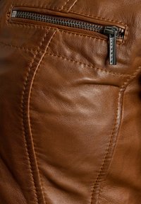 Sectie van een bruine leren jack met een ritszak, gedetailleerde stiksels en een gladde textuur. De rits heeft een metallic afwerking.