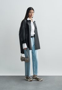 Black leather oversized shirt, white collared shirt underneath, light blue straight-leg jeans, gray and white sneakers, small gray handbag.