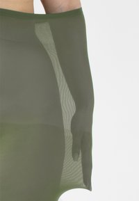 Collant trasparenti verde oliva con una texture liscia, dotati di una vita aderente e di un'opacità variabile lungo la gamba.