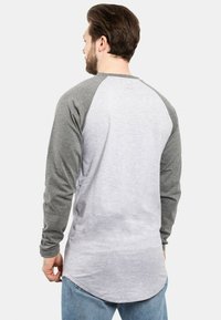 Langärmliges Hemd mit grauen Ärmeln und einem helleren grauen Körper, mit abgerundetem Saum und dezentem Logodetail auf dem Rücken. Material aus Baumwollmischung.