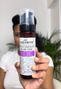 CurlSmith Bouncy Strength Volume Foam in een heldere fles met een zwarte pomp. Het etiket heeft zwart-witte tekst met paarse accenten en een bloemontwerp.