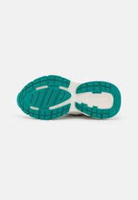 Semelle de chaussure avec une base blanche et un motif de traction en caoutchouc teal. Comprend des rainures et des crêtes pour l'adhérence et la flexibilité.