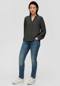 Blouse grise à manches longues avec un motif subtil et un décolleté en V, associée à un jean bleu et des baskets blanches.