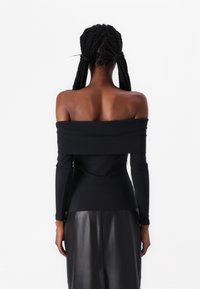Crna majica s off-the-shoulder izrezom i dugim rukavima, izrađena od glatkog materijala. Ima uski kroj i široki izrez, u kombinaciji s kožnom suknjom.