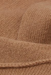 Brauner Strickstoff mit einer weichen, strukturierten Oberfläche. Das Material ist dick und weist ein geripptes Muster sowie dezente Nähte entlang der Kante auf.