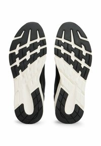 Vista della suola di scarpe sportive bianche e nere con battistrada a motivo progettato per la trazione e la durata.