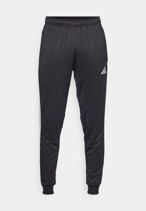 Pantalones deportivos negros con una textura suave, cinturilla elástica y piernas acampanadas. Cuenta con un logo blanco de Adidas y franjas laterales.