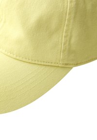 Gros plan sur une casquette de baseball en tissu jaune clair montrant les détails de la couture sur la calotte et la visière incurvée.