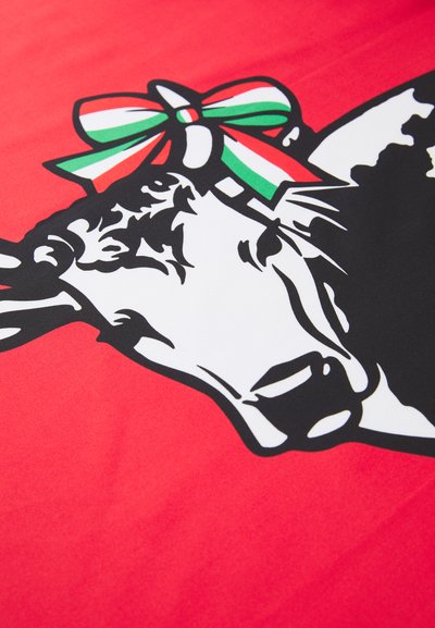 Sarkans fons ar baltu un melnu govs galvas dizainu, apdarinātu ar zaļu, baltu un sarkanu lentīti virsū.