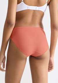 Højtaljede koralfarvede undertøj lavet af glat stof med en blød, elastisk taljebånd og minimale syningsdetaljer for komfort.