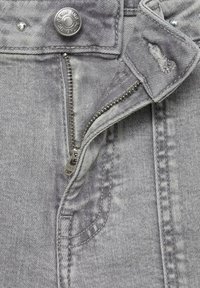 Zip grigio in denim con tirante metallico, chiusura con bottone e dettagli di tasca cucita. Texture leggermente rovinata e finitura sbiadita.