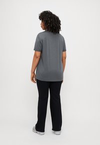 Gray short-sleeve t-shirt with a round neck, paired with black flare pants and gray footwear, viewed from the back. Smooth fabric texture.