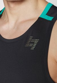 Top de entrenamiento negro con acentos turquesas, que presenta una tela texturizada y un logo reflectante en el pecho. Diseño ajustado.