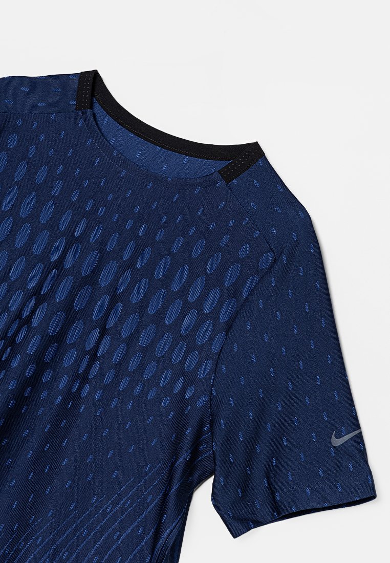 Maglietta sportiva blu navy con colletto rotondo, caratterizzata da una texture liscia e un motivo a pois, accentuata da un colletto nero e un piccolo logo.