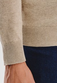Beżowy sweter z dzianiny z bliska, z prążkowanymi mankietami i dołem, o miękkiej teksturze; w zestawie z ciemnoniebieskim denimu.