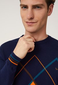 Maglione blu navy con motivi geometrici in arancione, turchese e marrone. Polsini a costine con strisce a contrasto. Texture morbida, design a girocollo.