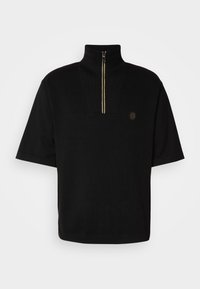 Černý pulovr s krátkým rukávem, s vysokým límcem, s polovičním zipovým uzavřením a malým logem na hrudi. Vyrobeno z texturované látky.