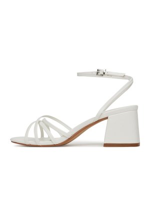 Valged plokknõudega sandaalid kitsaste krõssõlgadega, sääreluu rihm metallist pandlaga ja tekstureeritud tallaga. Tasane varvaku disain.