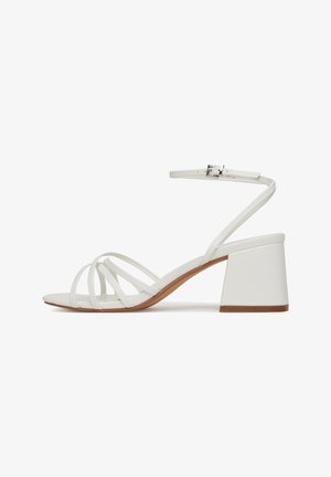 Sandale albe cu toc bloc, cu curele subțiri în cruce, curea pentru gleznă cu cataramă din metal și talpă texturată. Design plat pentru degete.
