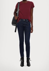 Camiseta corta de color burdeos combinada con jeans skinny de color azul oscuro. Botines negros con cordones. Modelo sosteniendo un bolso negro.