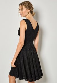 Czarna koronkowa sukienka z bezrękawowym fasonem, rozkloszowanym dołem i dekoltem w kształcie litery V na plecach. Teksturowany materiał z dopasowaną górą i ukrytą zasuwaką.