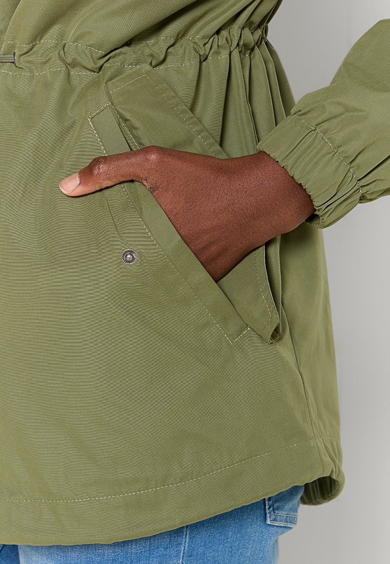 Zielona, lekka kurtka z teksturowanym wykończeniem, elastycznym pasem i kieszeniami bocznymi. Posiada mankiety na rękawach oraz minimalne detale z metalu.